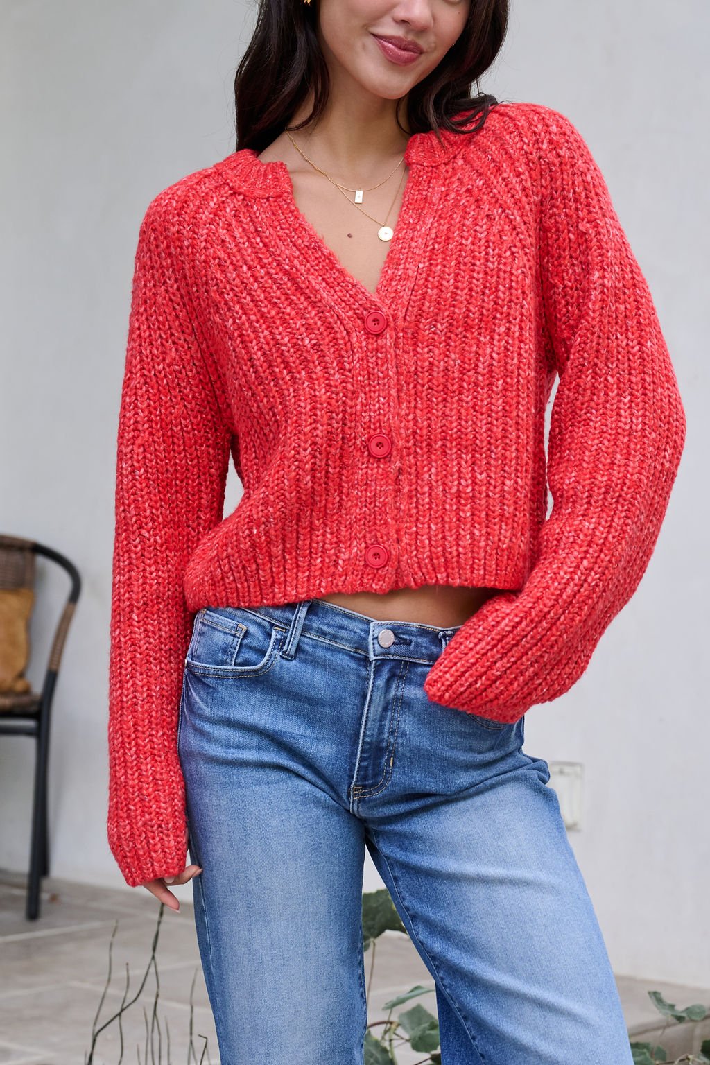 Woman in a Red Confetti Knit Buttoned Cardigan and blue jeans, standing indoors with a faint smile and relaxed pose.