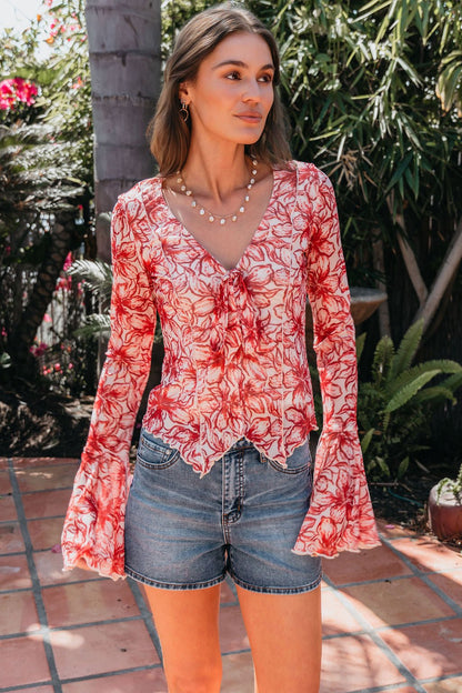 Woman wears the Red Floral Print Bell Sleeve Mesh Top with denim shorts on a patio surrounded by greenery.
