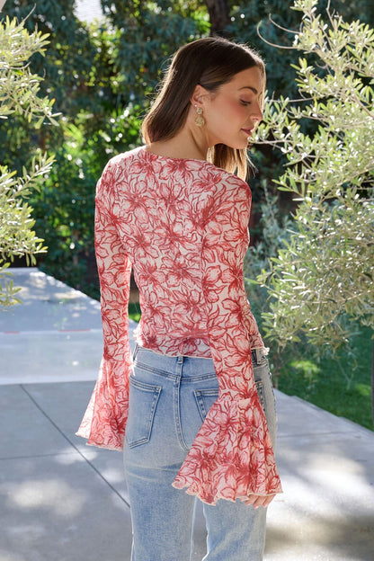 A woman outdoors, facing away, wearing a Red Floral Print Bell Sleeve Mesh Top with light blue jeans.