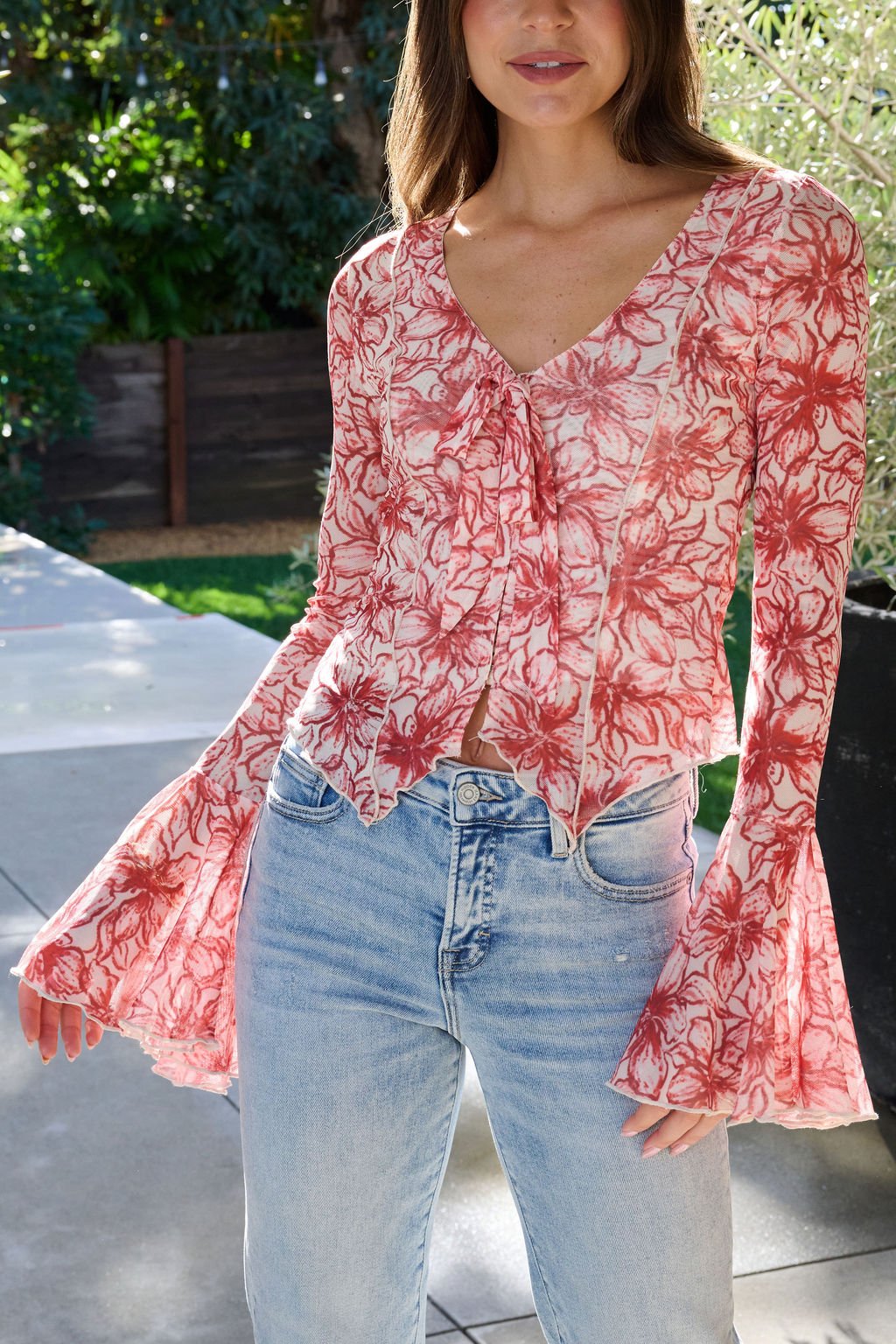 Woman wearing a Red Floral Print Bell Sleeve Mesh Top and light blue jeans, standing outdoors in sunlight.