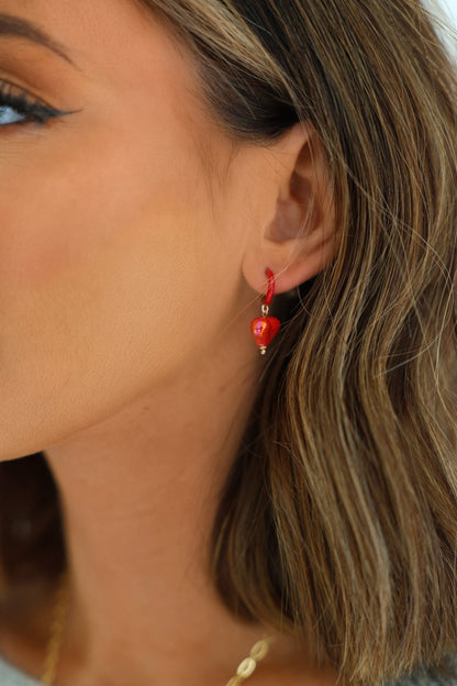 Close-up of a woman's ear wearing Red Heart Charm Hoop Earrings; she has shoulder-length brown hair with blonde highlights.