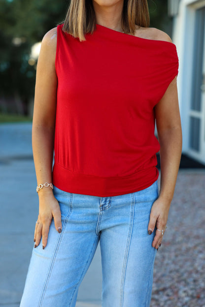 Woman wearing a Red Jersey Knit Off The Shoulder Top (Pre Order) and light blue jeans, standing outdoors with hands by her sides.
