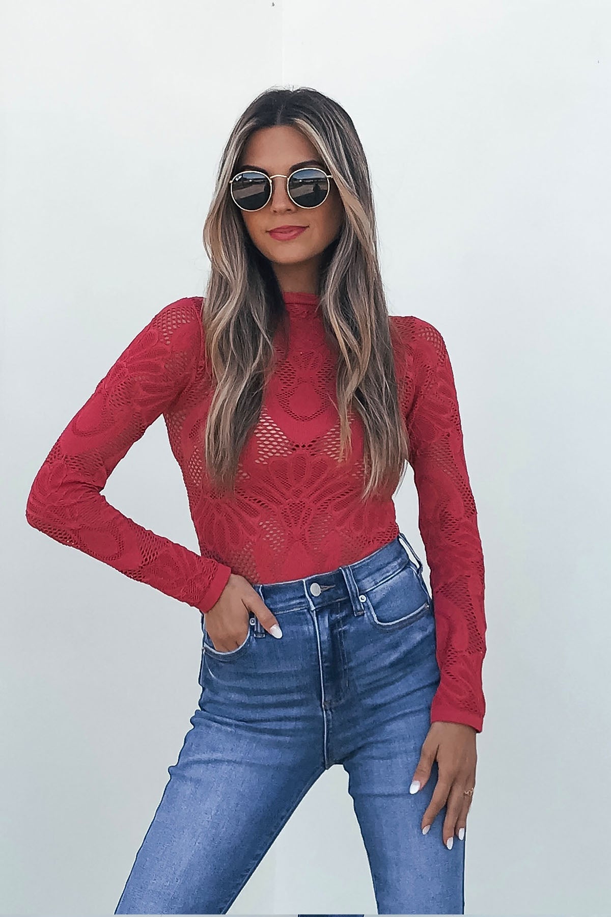 Woman styles the Red Mock Neck Fishnet Top - FINAL SALE with high-waisted jeans, wavy hair, and sunglasses against a plain background.