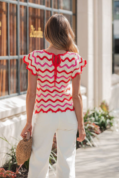 Woman outdoors in a Red Multi Chevron Knit Sweater with white pants and a woven bag, facing away from the camera.