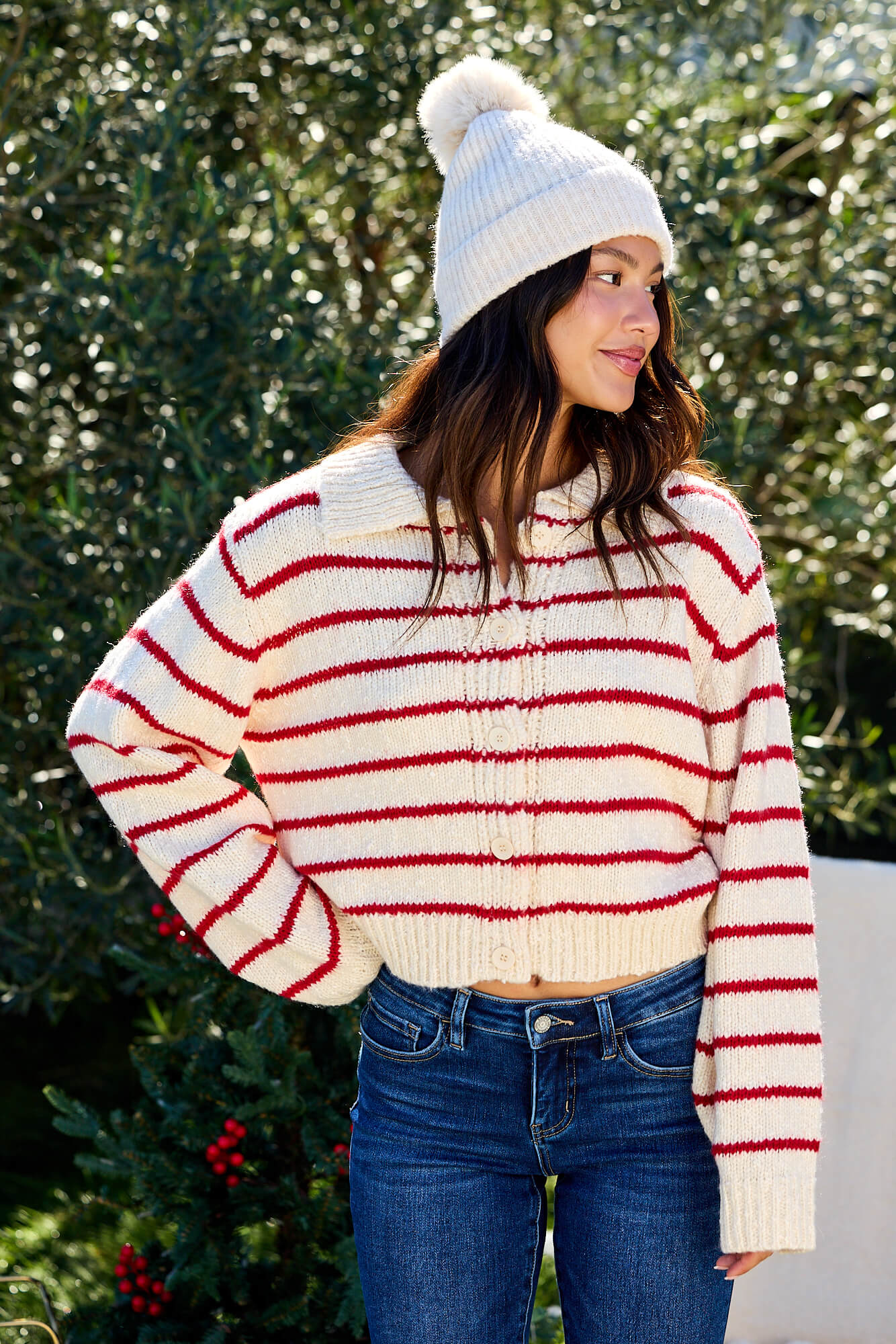 A woman in a Red Striped Button Down Knit Cardigan - FINAL SALE smiles outdoors, framed by lush greenery.