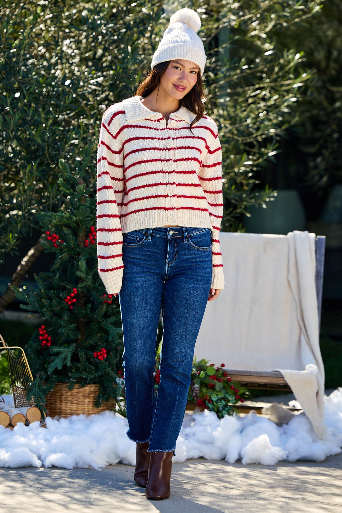 Woman wears the Red Striped Button Down Knit Cardigan - FINAL SALE with jeans and boots outdoors near faux snow and greenery.