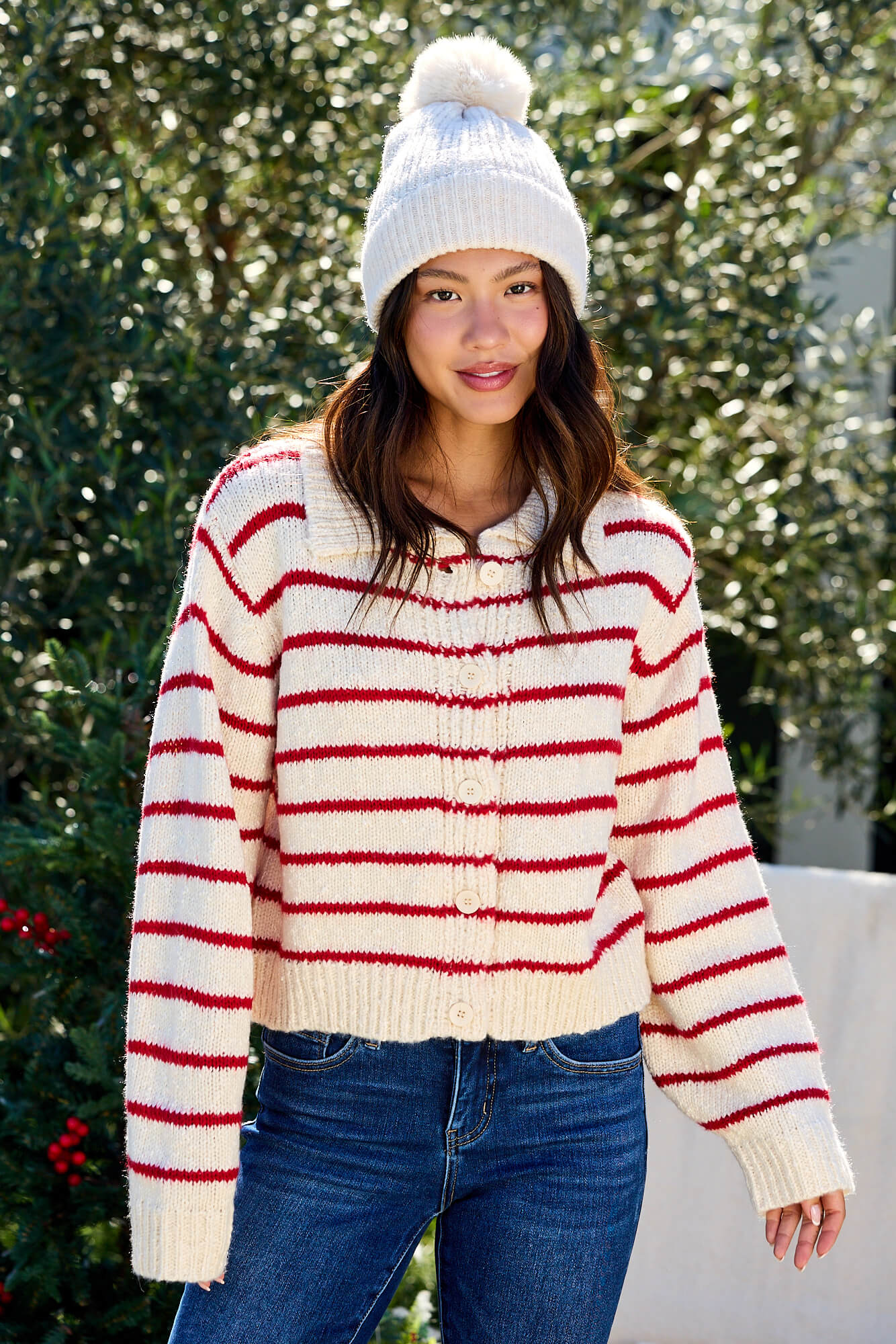 Woman smiles outdoors wearing the Red Striped Button Down Knit Cardigan - FINAL SALE, paired with jeans and a white beanie.