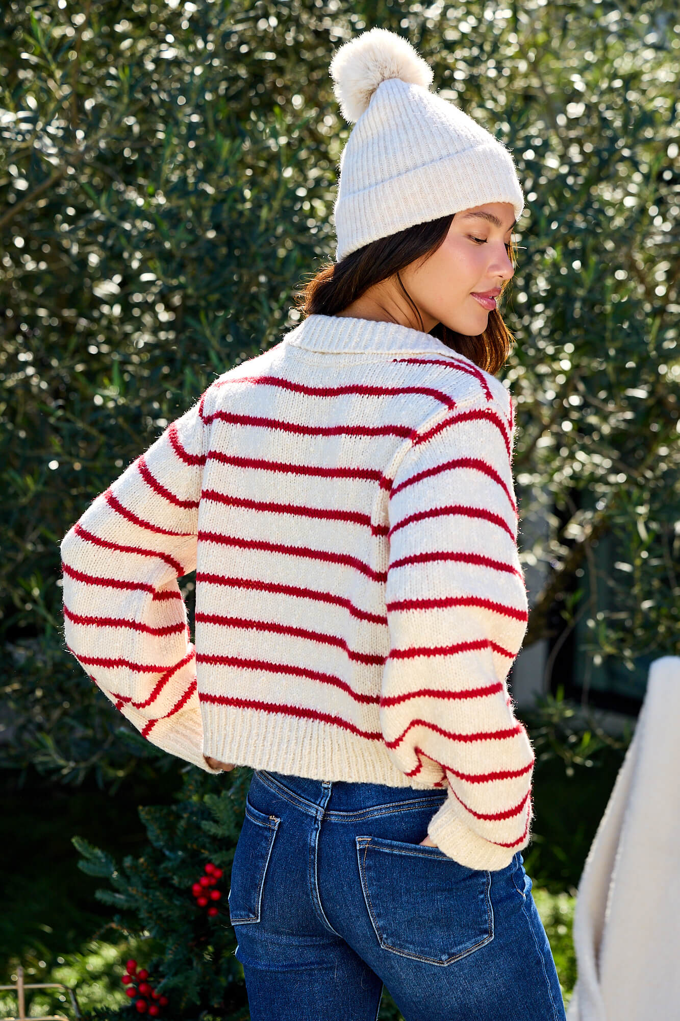 A woman outdoors wears the Red Striped Button Down Knit Cardigan - FINAL SALE, facing away and looking over her shoulder.