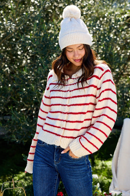 A woman in the Red Striped Button Down Knit Cardigan - FINAL SALE stands outdoors, smiling softly with a hand in her jeans pocket.