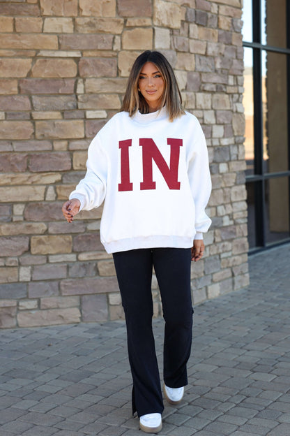 A woman shows Hoosier pride in a Reversible Indiana Pullover Sweatshirt, smiling as she walks by a brick wall.