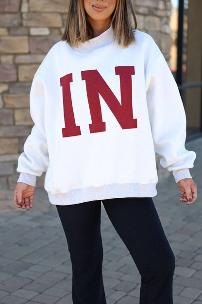 Woman outdoors in a Reversible Indiana Pullover Sweatshirt with bold red IN letters, showing Hoosier pride by a stone wall.