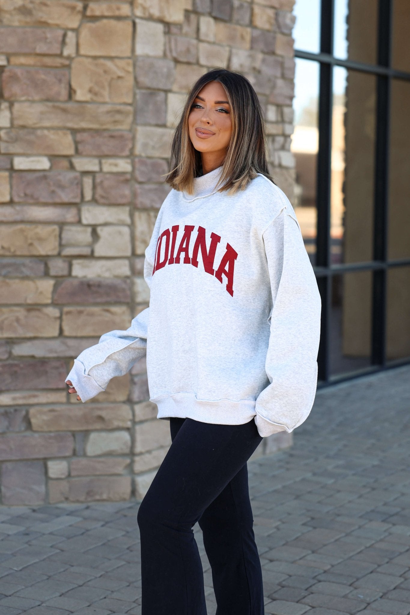 Woman outside a stone building, smiling with Hoosier pride in a Reversible Indiana Pullover Sweatshirt and black pants.