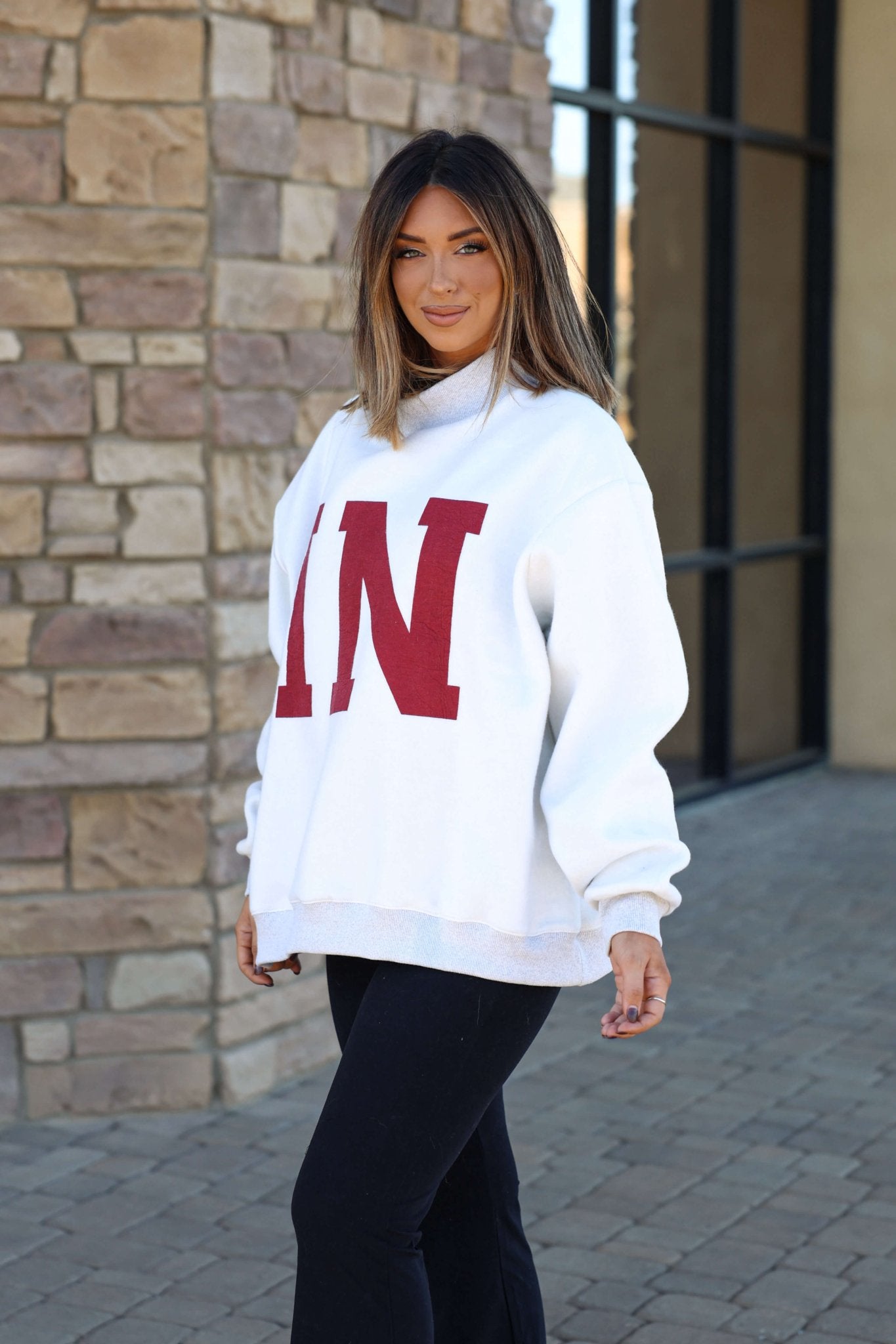 Woman with straight hair wears a Reversible Indiana Pullover Sweatshirt and black pants, standing on a stone walkway.