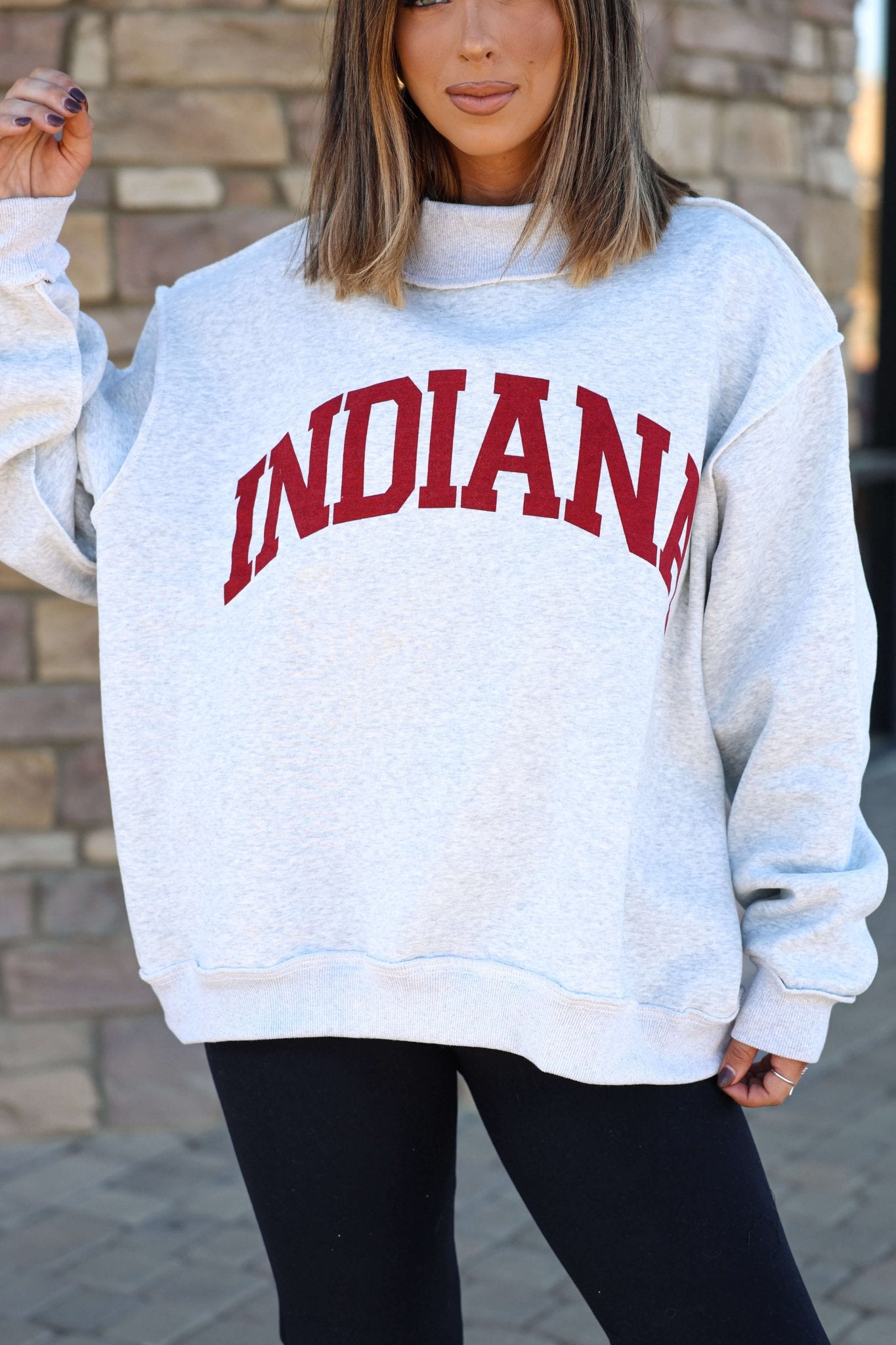 Woman sports a Reversible Indiana Pullover Sweatshirt with red letters, standing by a stone wall and showing Hoosier pride.