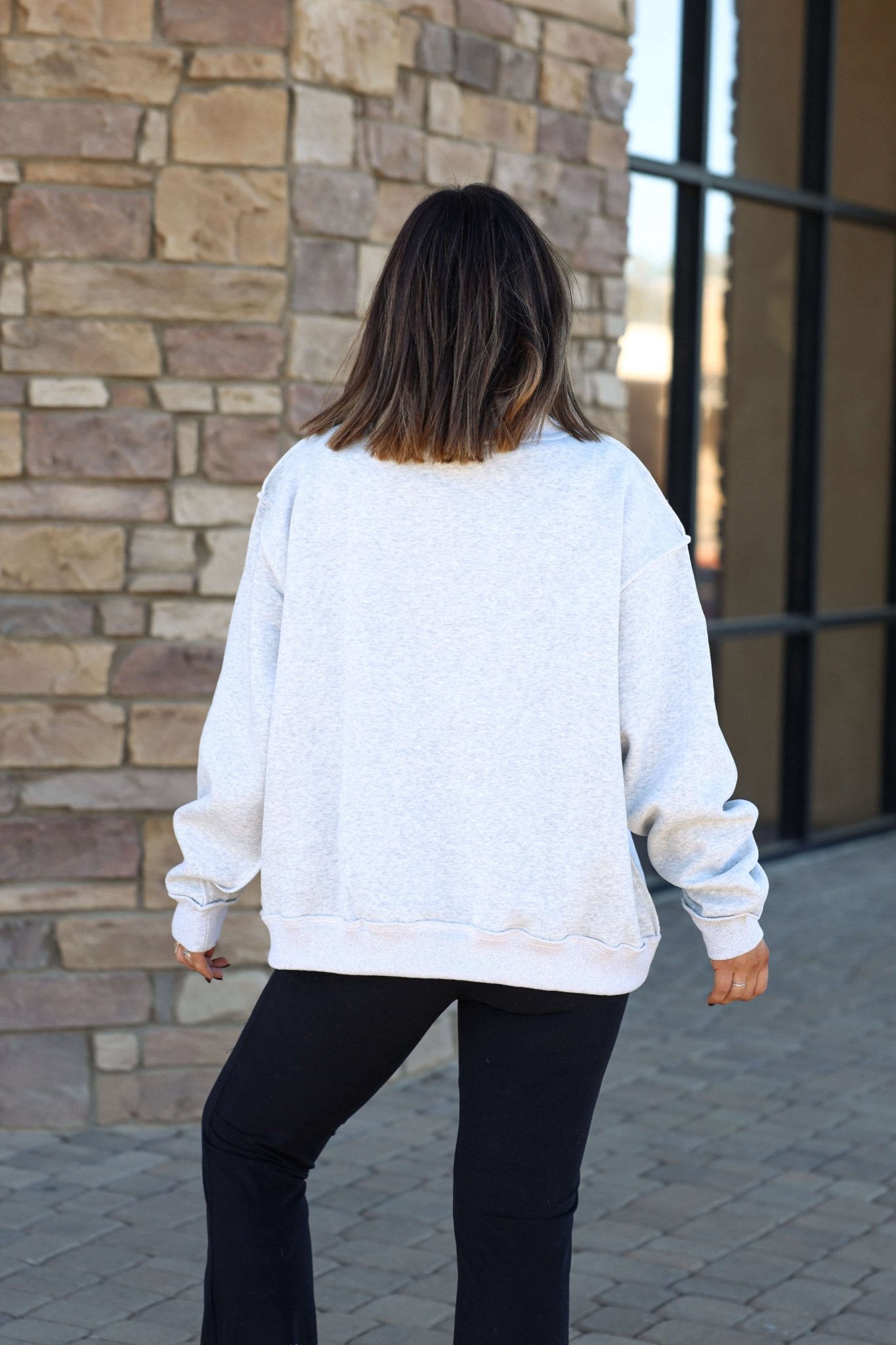A person in a Reversible Indiana Pullover Sweatshirt and black pants stands outdoors facing a brick wall.