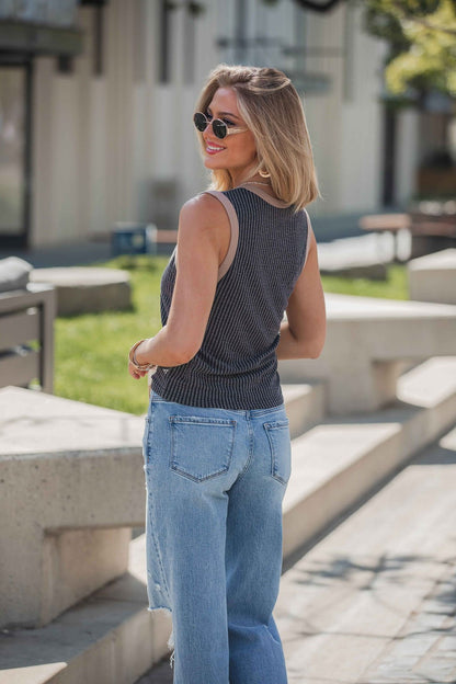 A woman in sunglasses and blue jeans smiles outdoors, wearing a Ribbed Contrast Trim Tank Top - Black, looking over her shoulder.
