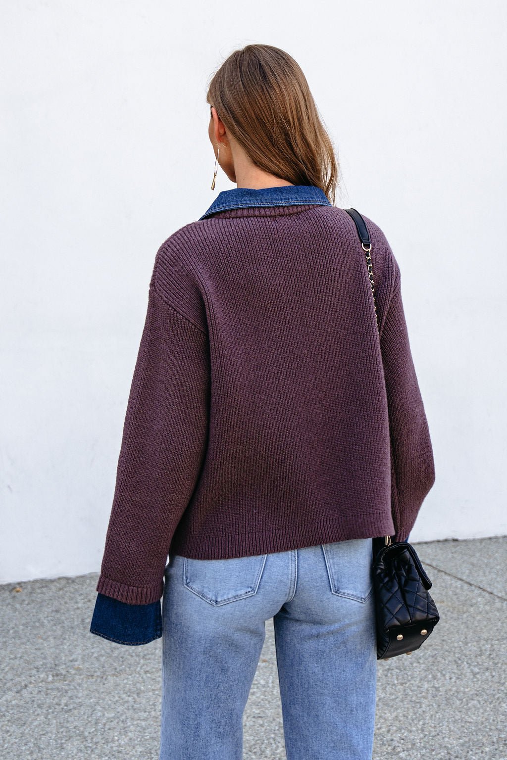 Woman with long brown hair in a Ribbed Denim Contrast Sweater - Mocha, jeans, and black purse, back to camera.
