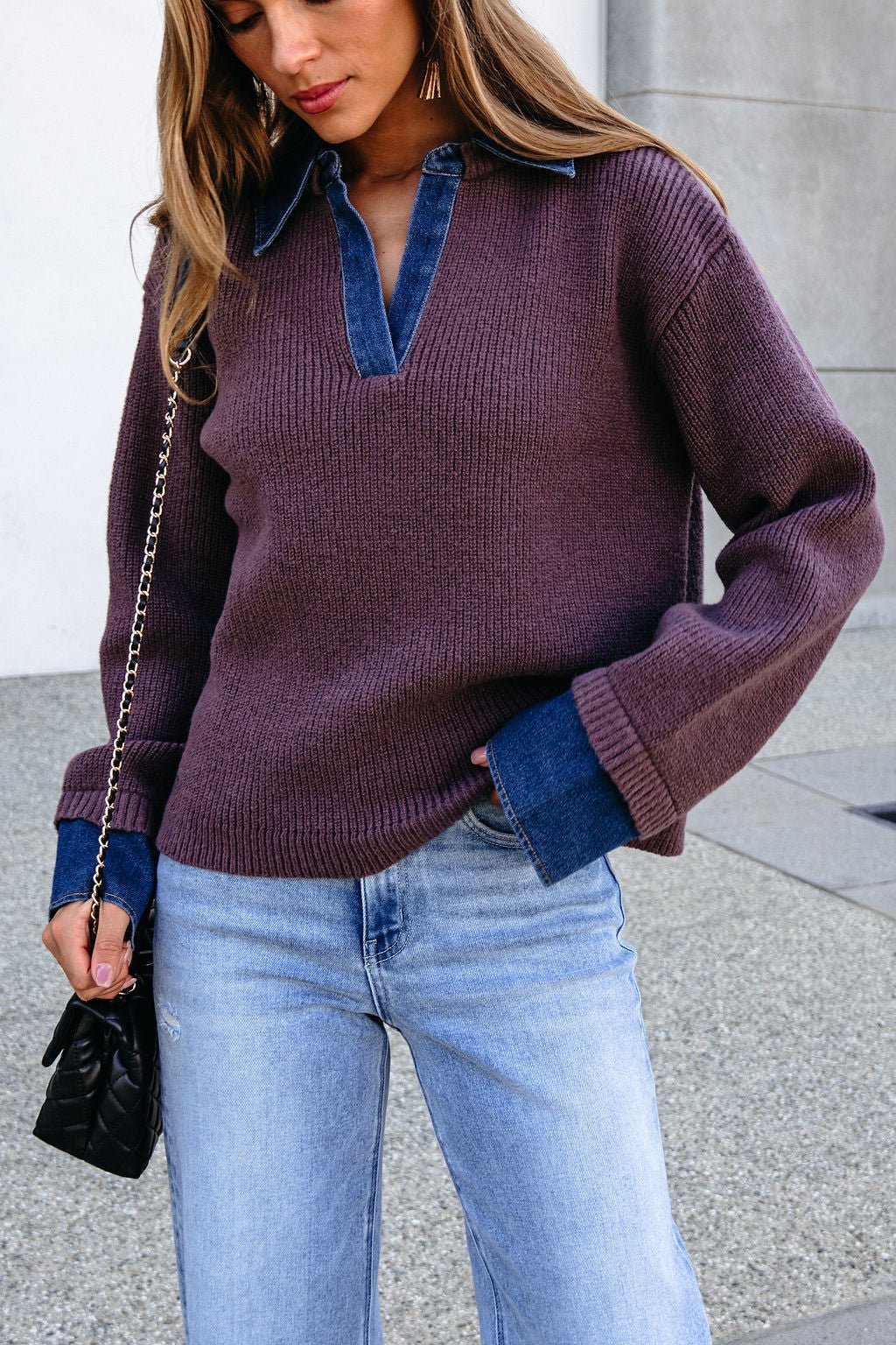 Woman in a Ribbed Denim Contrast Sweater - Mocha over a blue shirt, light jeans, and carrying a small black quilted bag.