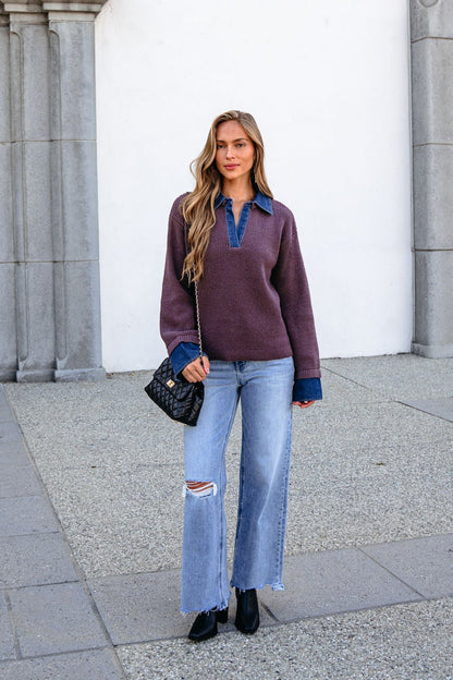 Woman in a ribbed denim contrast sweater (mocha), denim shirt, ripped jeans, black boots, holds a quilted black purse outside.