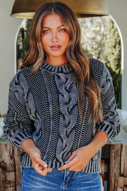 Woman with long brown hair wearing the Riley Charcoal Cable Knit Sweater and blue jeans, standing outdoors in natural light.