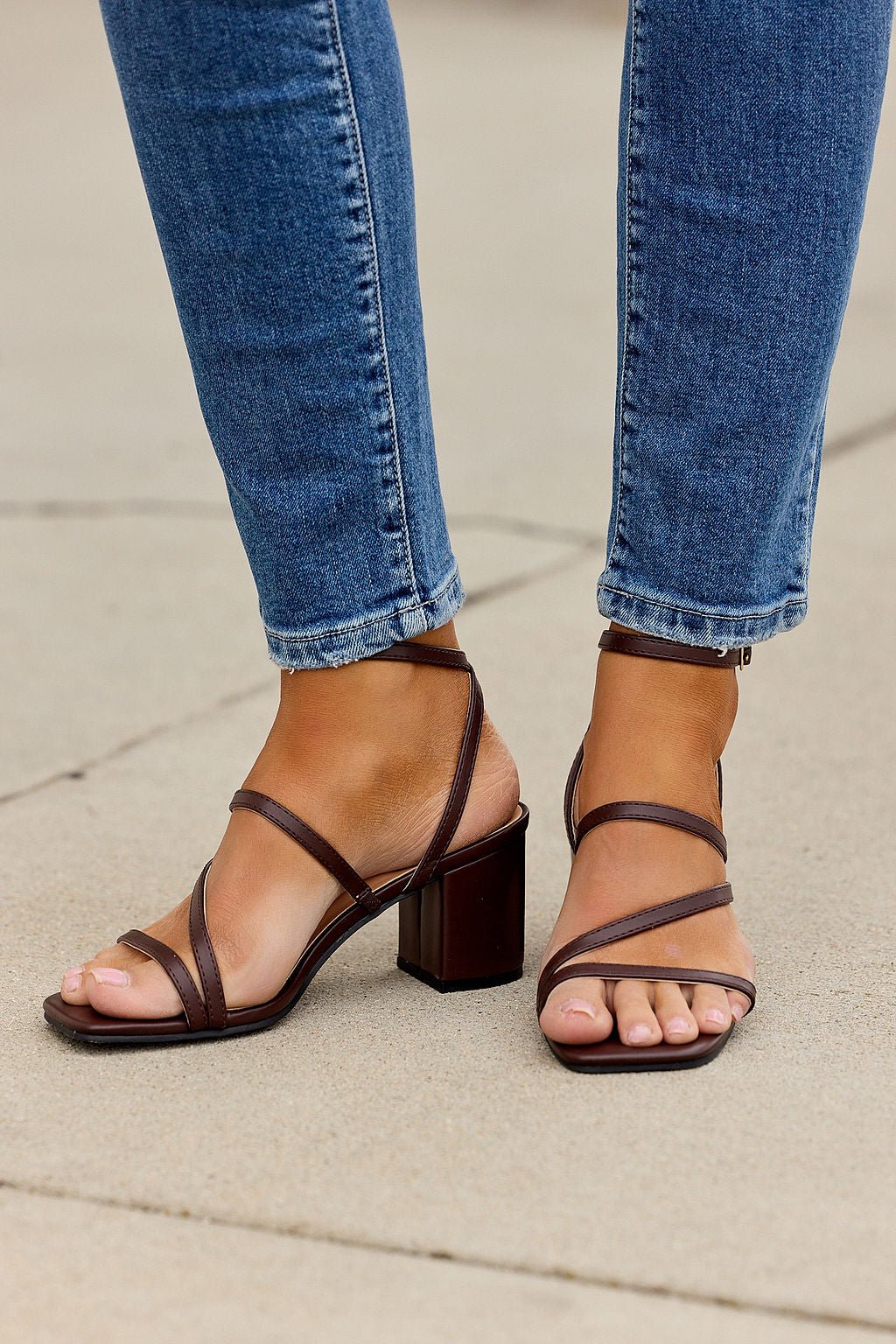 Person wearing blue jeans and Roma Strappy Block Heels - Brown, standing on a concrete surface.