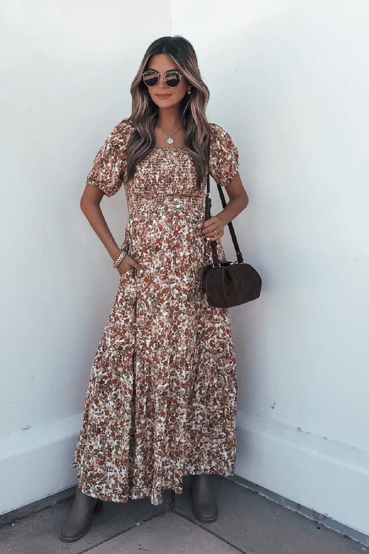 Woman in sunglasses wears a Rust Floral Print Midi Dress with brown boots and a dark brown bag, standing against a white wall.