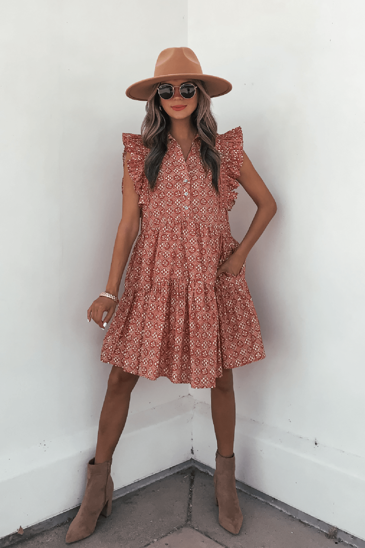 Woman in Rust Print Flutter Sleeve Mini Dress - FINAL SALE, tan hat, boots & sunglasses, standing by a white wall.