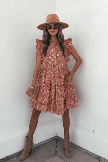 Woman in Rust Print Flutter Sleeve Mini Dress - FINAL SALE, tan hat, boots & sunglasses, standing by a white wall.