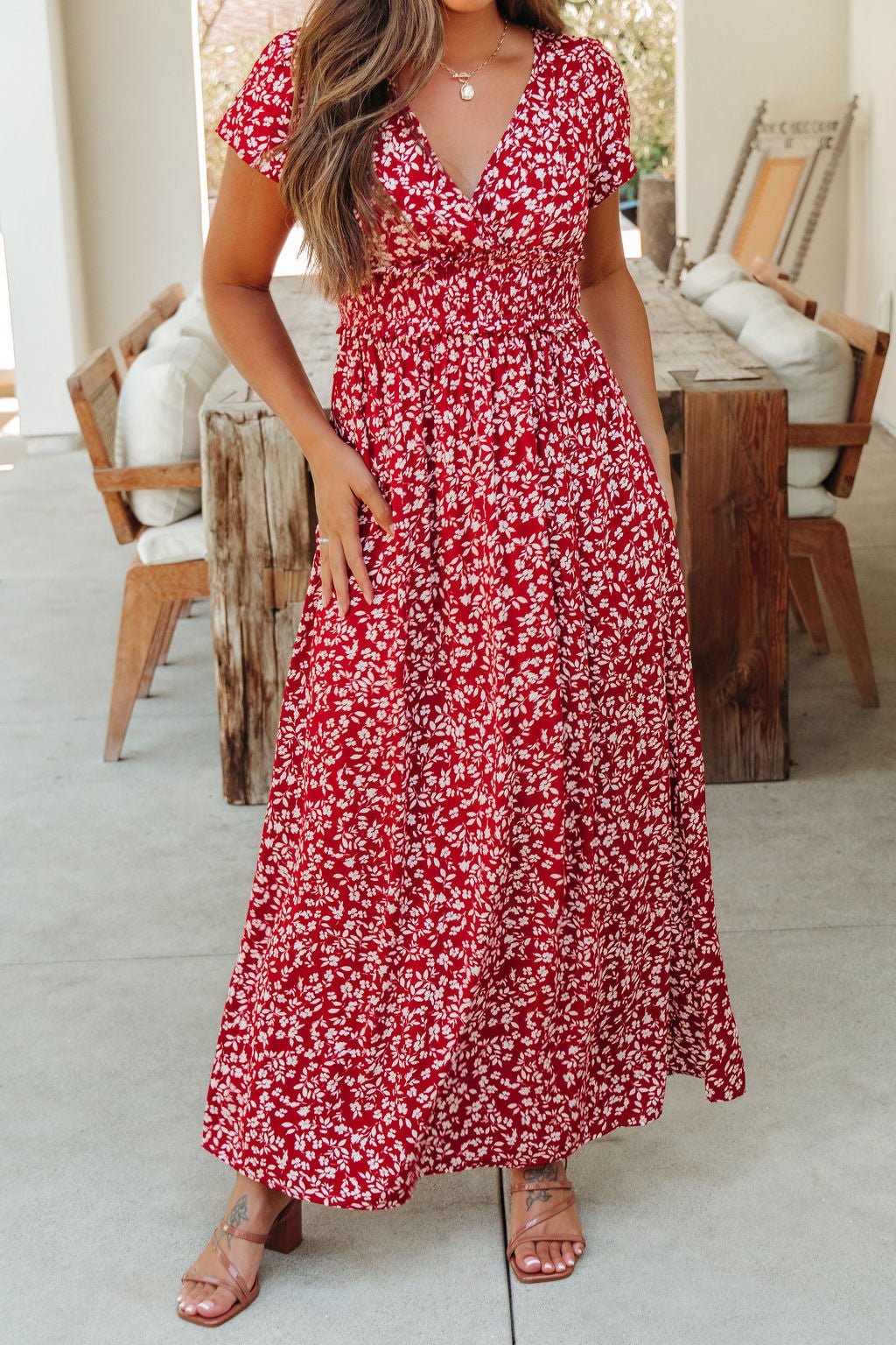 Woman wearing the Sabrina Red and White Floral Maxi Dress - DOORBUSTER, standing in a stylish outdoor seating area.