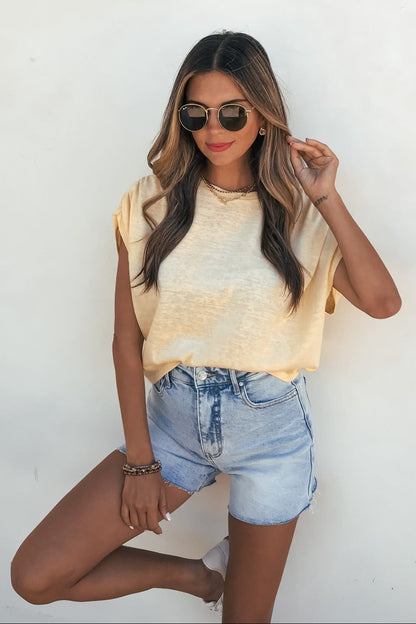 Woman in sunglasses and Sadie and Sage Marlow Gathered Top - Yellow poses by a white wall with one hand on her sunglasses.