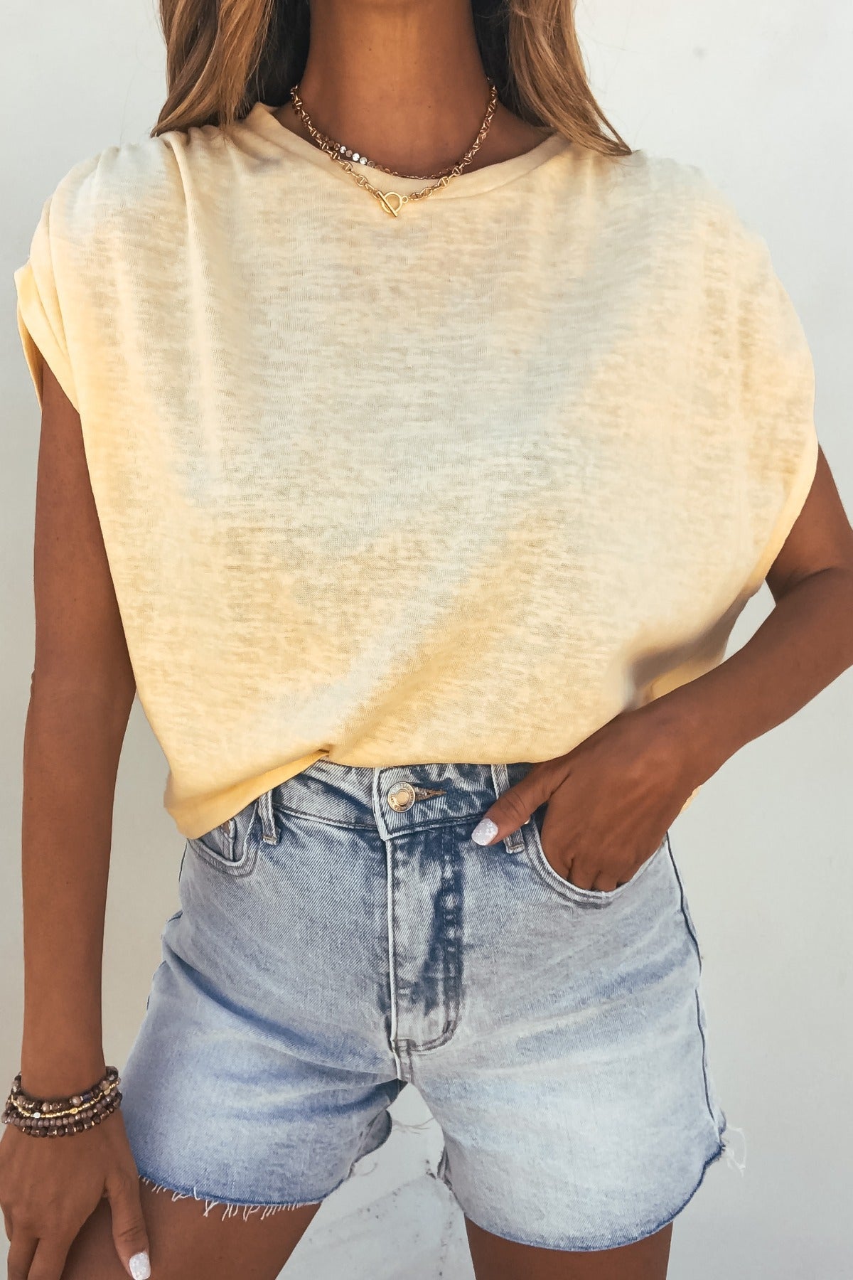 Woman wears the Sadie and Sage Marlow Gathered Top in yellow with high-waisted light denim shorts, hand in pocket, bracelets on wrist.