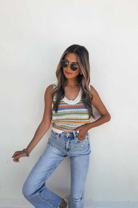 Woman in Sadie and Sage Stripe Knit Sweater Tank Top and light blue jeans stands against a plain white wall.