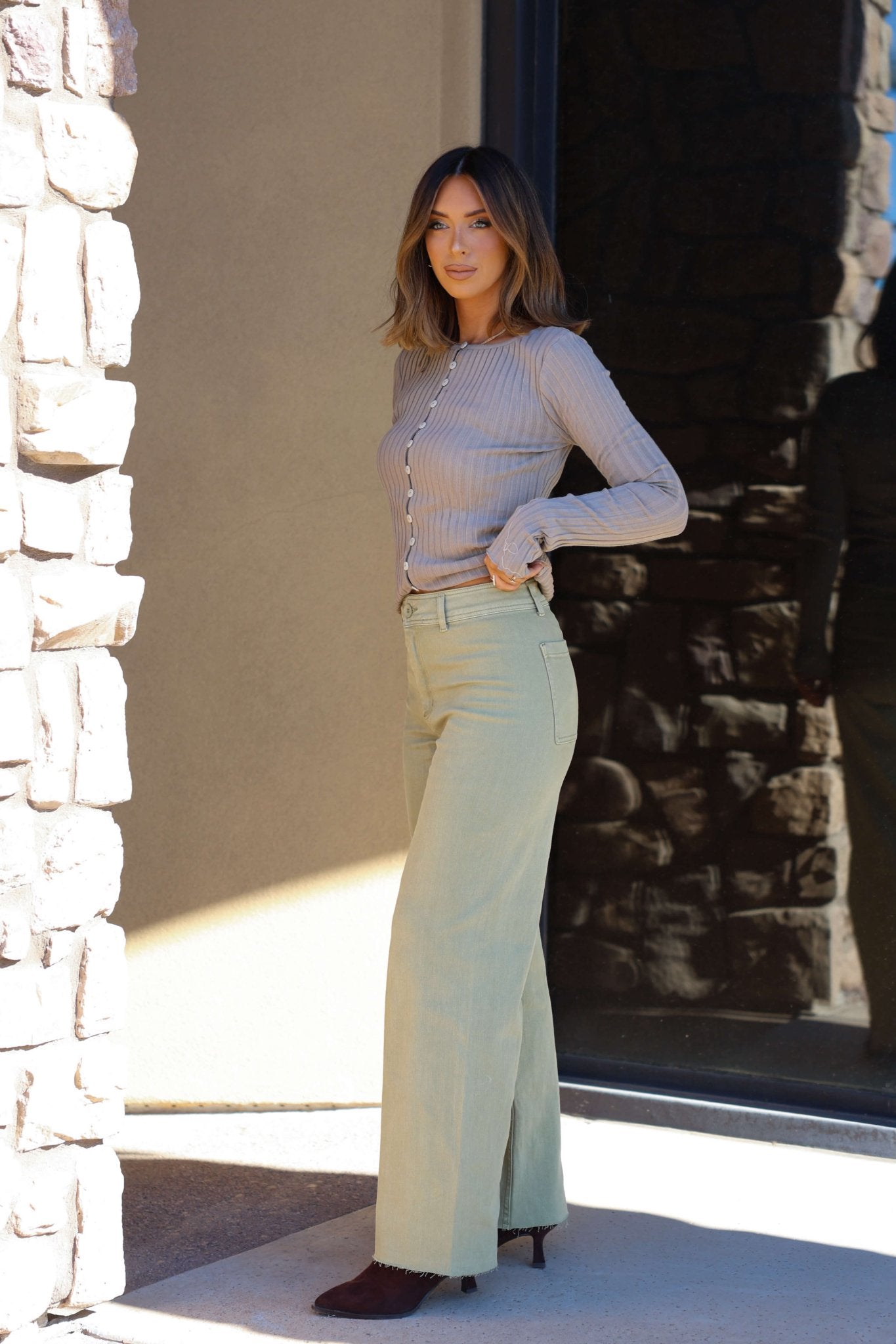 A woman stands by a stone wall, wearing ribbed top and Sage Straight Wide Leg Pants—a perfect casual day look—facing the camera.