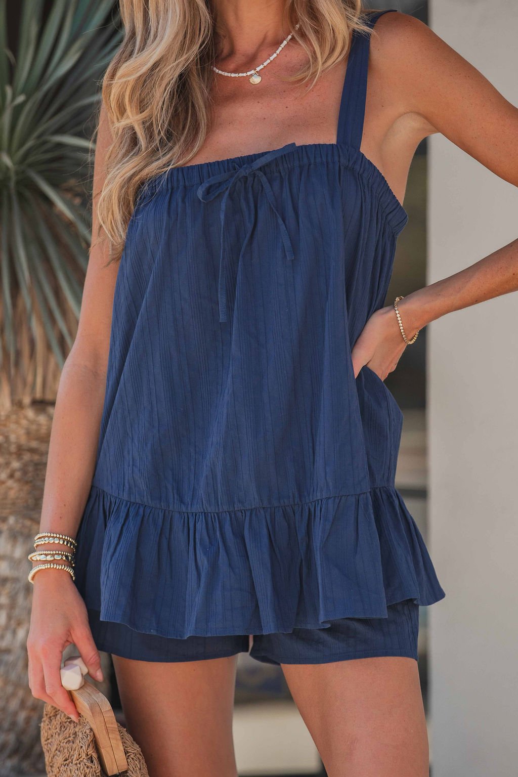 Woman in the Salt Air Navy Cami Set, 100% cotton loungewear, styled with bracelets and a woven bag.
