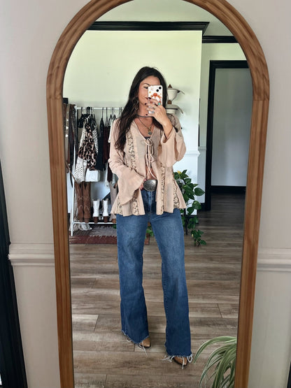Woman taking a mirror selfie in a Sand Bell Sleeve Sheer Lace Top and wide-leg jeans, clothes on a rack in the background.