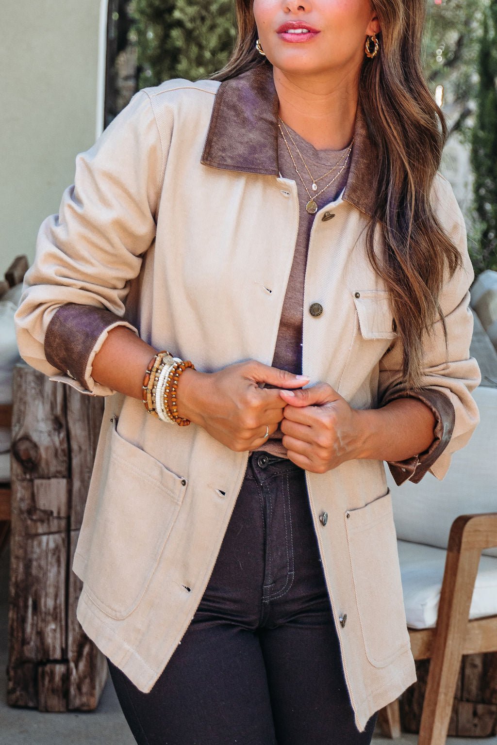 A woman wears the Sandstone Contrast Denim Shacket with a faux leather collar, dark jeans, and gold jewelry outdoors.