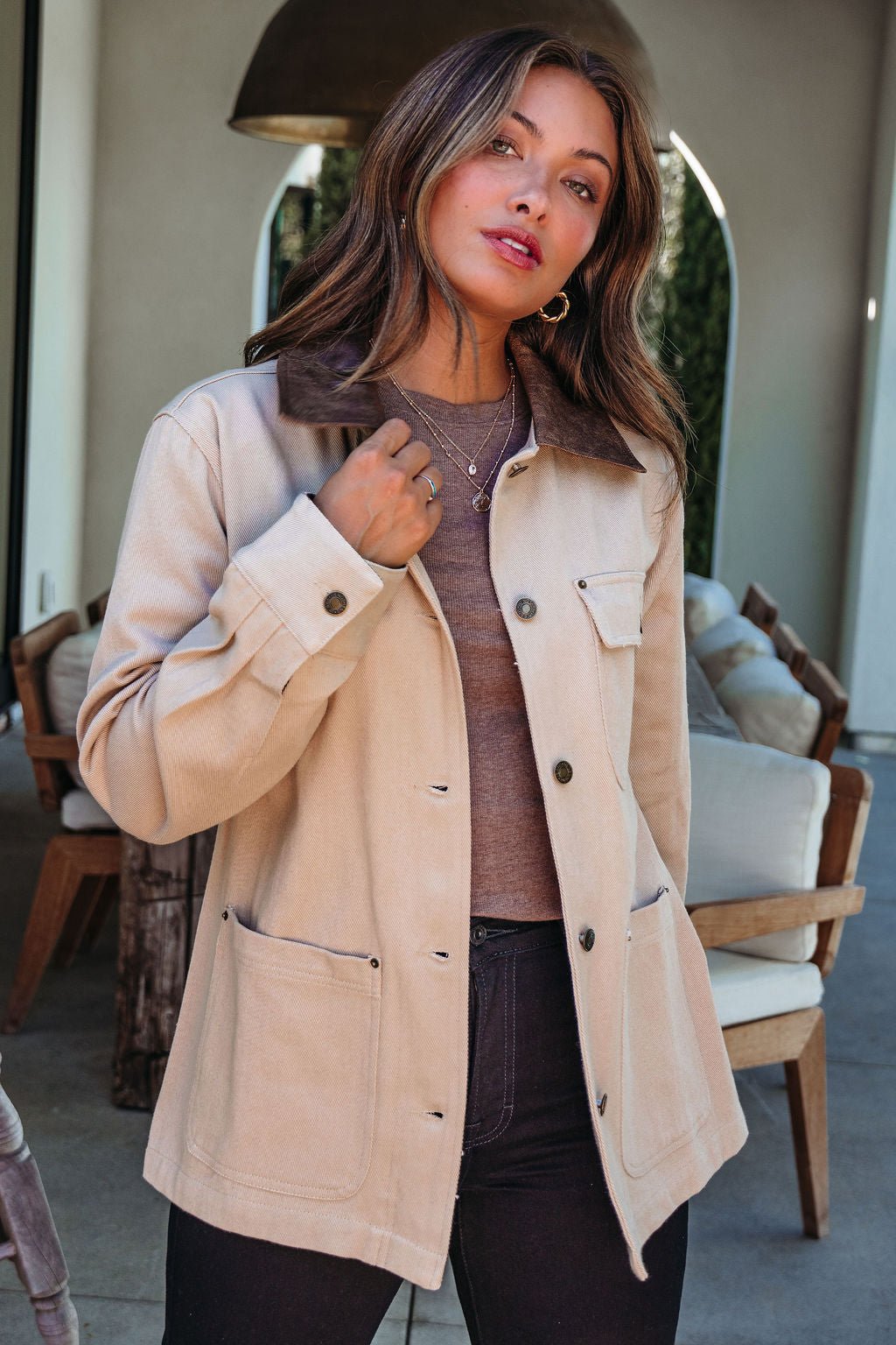 A woman wears the Sandstone Contrast Denim Shacket indoors, holding its collar and looking at the camera.