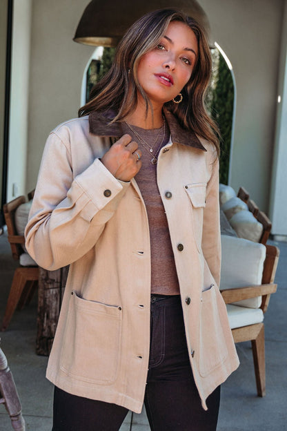 A woman wears the Sandstone Contrast Denim Shacket indoors, holding its collar and looking at the camera.