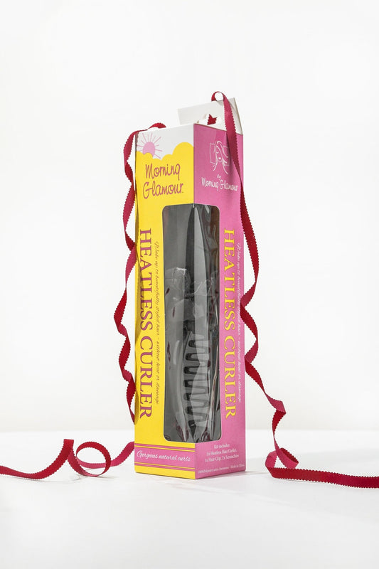 A pink and yellow box labeled Satin Heatless Hair Curler Kit - Black, with a black accessory and red ribbon beside it.