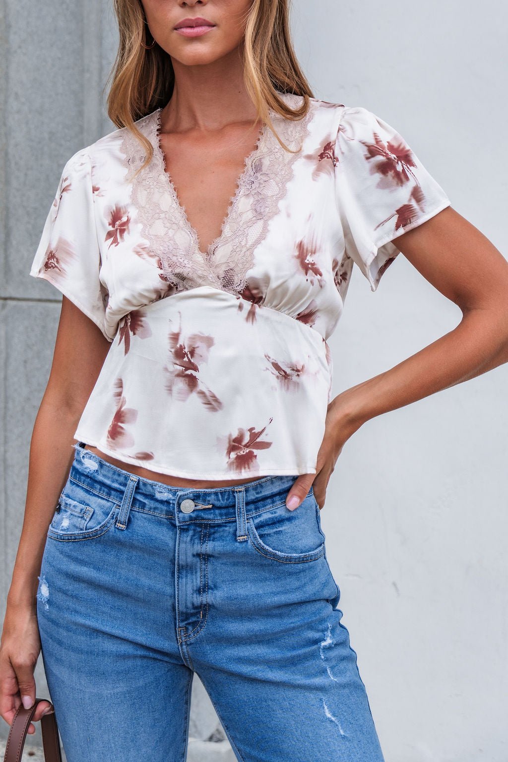 Woman in a Satin Lace Floral Print Top - Cream and blue jeans, standing against a light gray background.