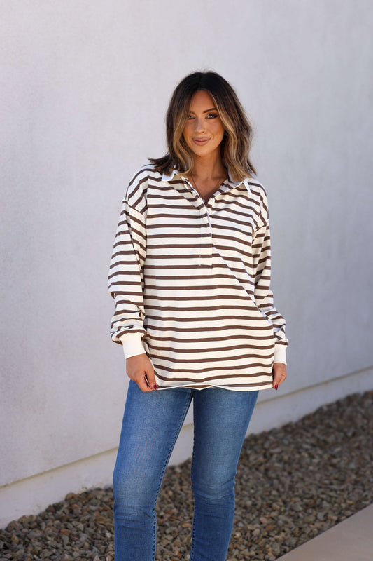 Woman in the Sawyer Brown Striped Pullover - DOORBUSTER and blue jeans stands on a stone path by a white wall, perfect for fall.