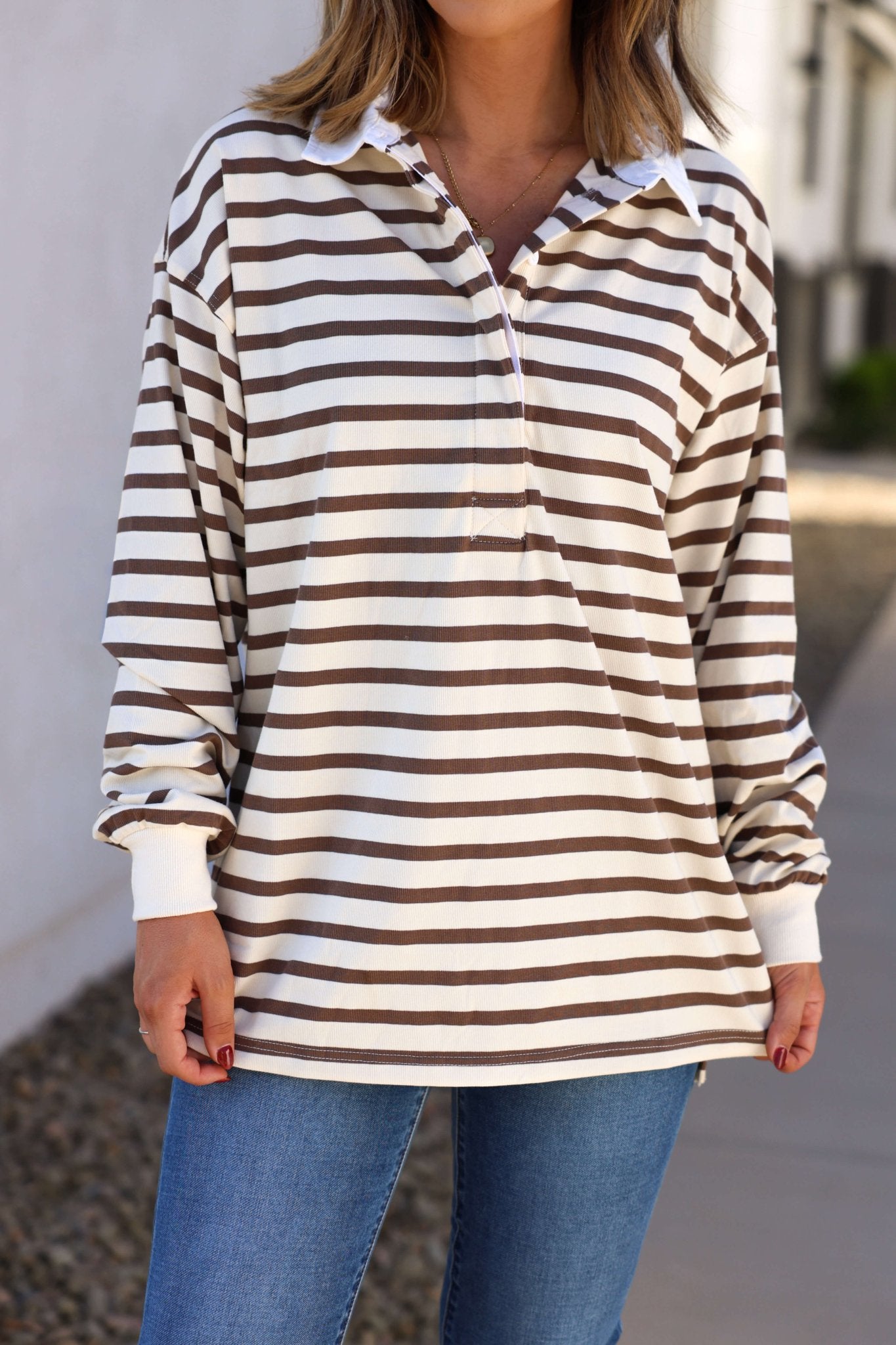 A person wears the Sawyer Brown Striped Pullover - DOORBUSTER with blue jeans outdoors—perfect for fall style.