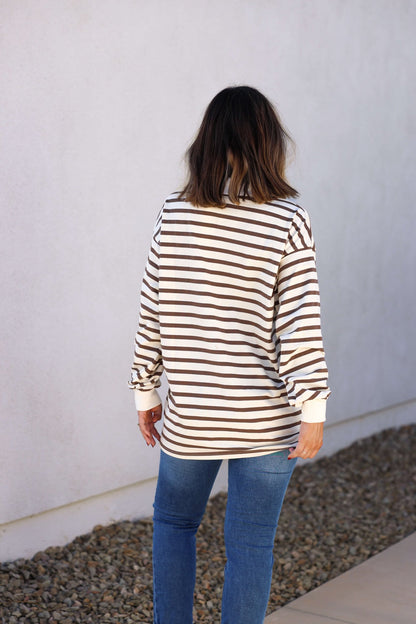 A person with shoulder-length hair faces away, wearing the Sawyer Brown Striped Pullover—an ideal fall styling piece.