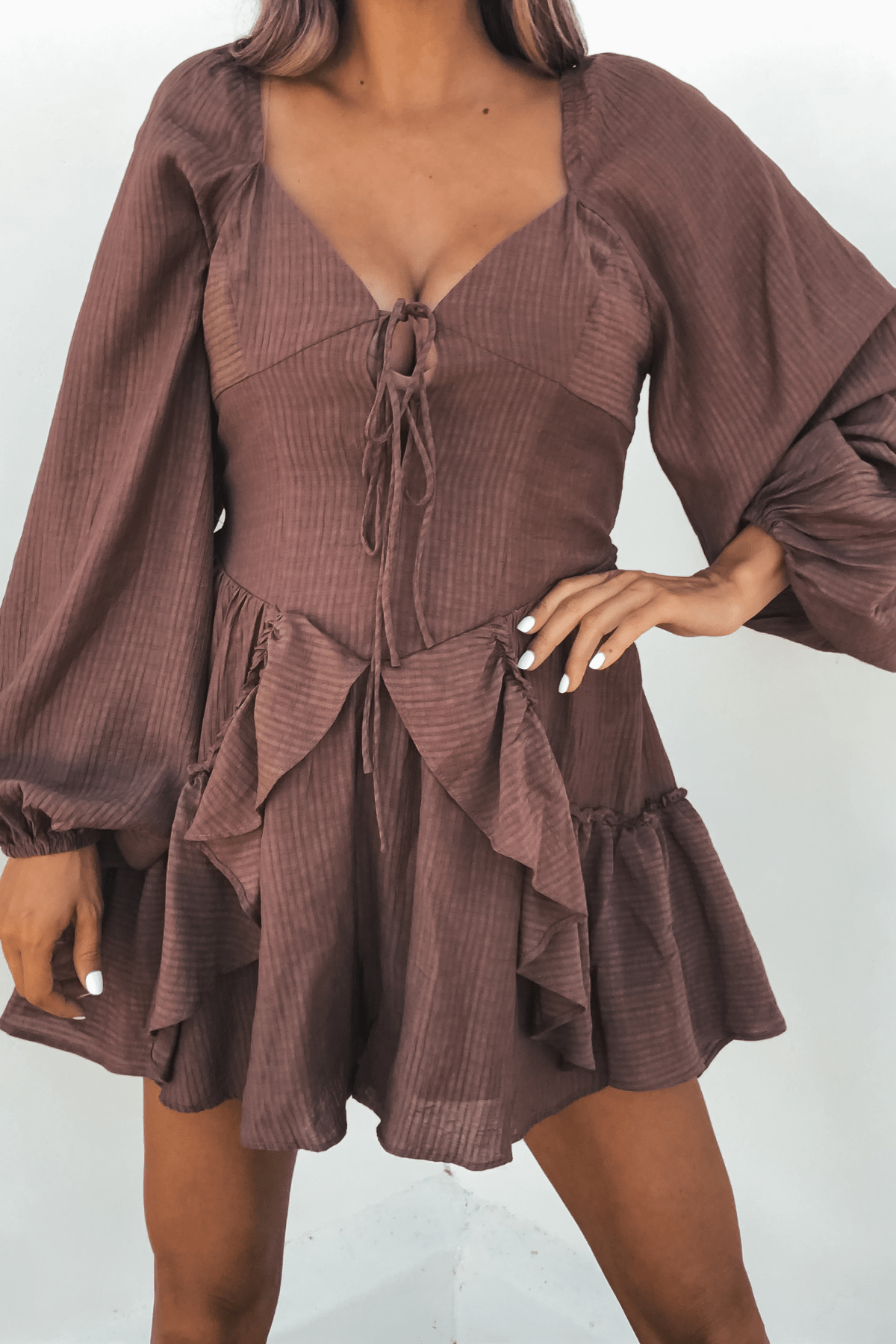 Woman wearing the Shay Mocha Ruffled Sweetheart Romper, a brown one-piece with tie-front, against a light background.