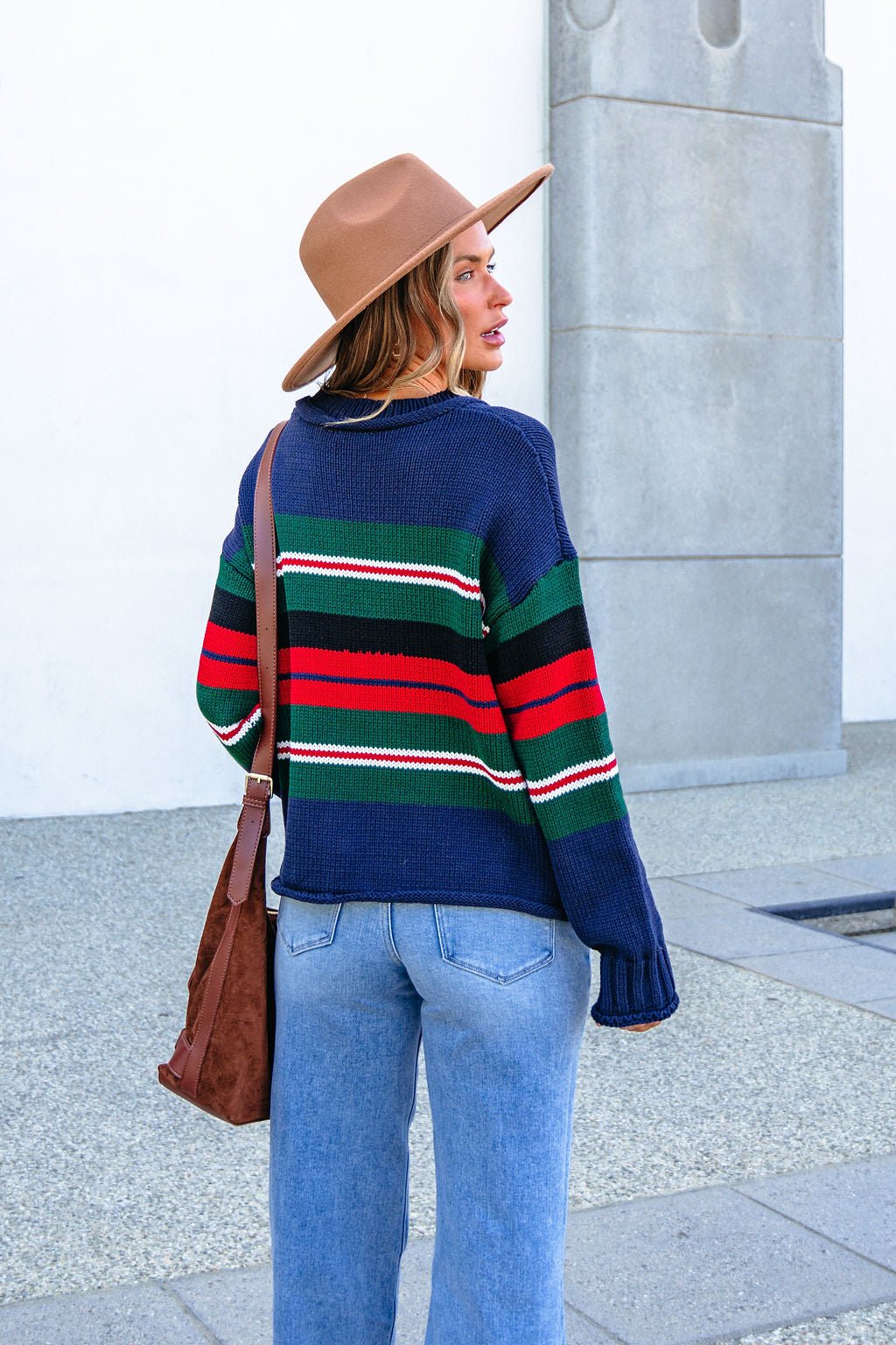 Woman faces away outside, wearing SHE AND SKY ST1207 navy striped sweater, tan hat, and blue jeans on a paved surface.