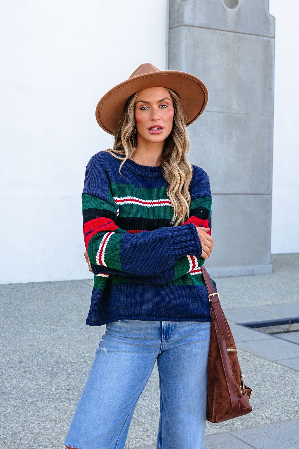 Woman in SHE AND SKY ST1207 navy striped sweater, wide-brim hat, jeans, and brown bag stands outdoors.