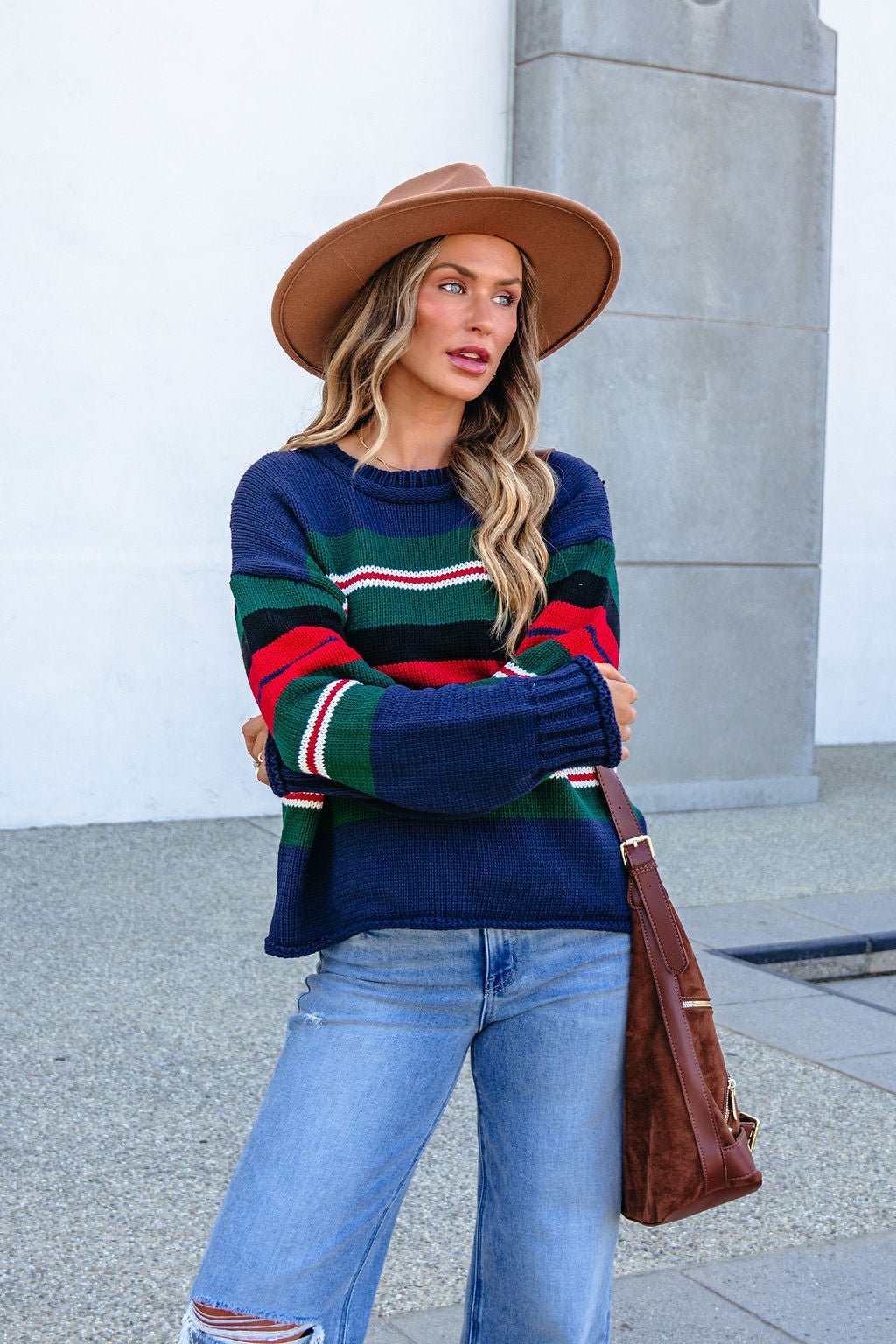 Woman outdoors in SHE AND SKY ST1207 navy striped sweater, jeans, brown hat, and brown bag, looking to the side.
