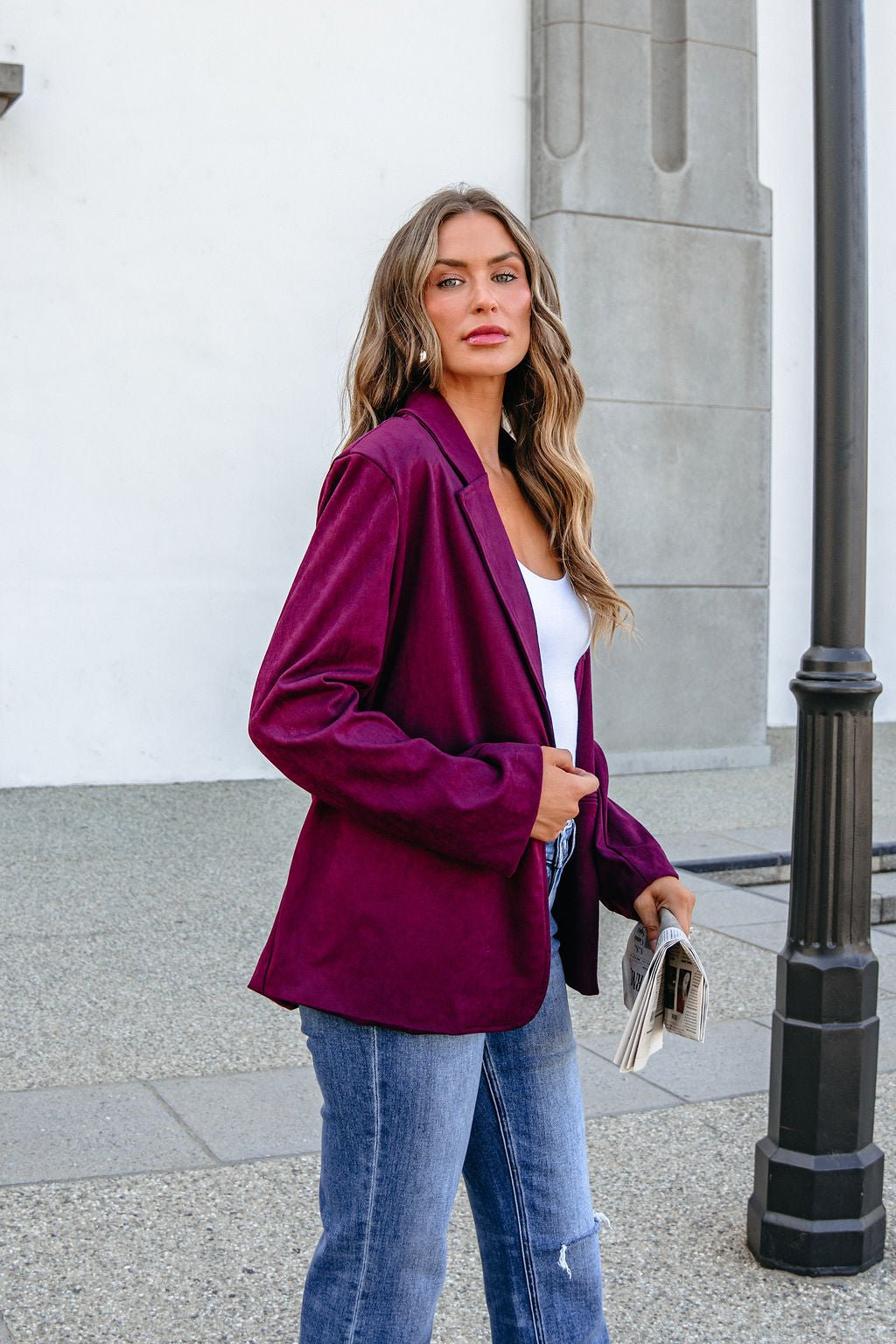 Woman in a SHE AND SKY ST1741 Wine Suede Oversized Blazer stands outdoors with a newspaper, looking at the camera.