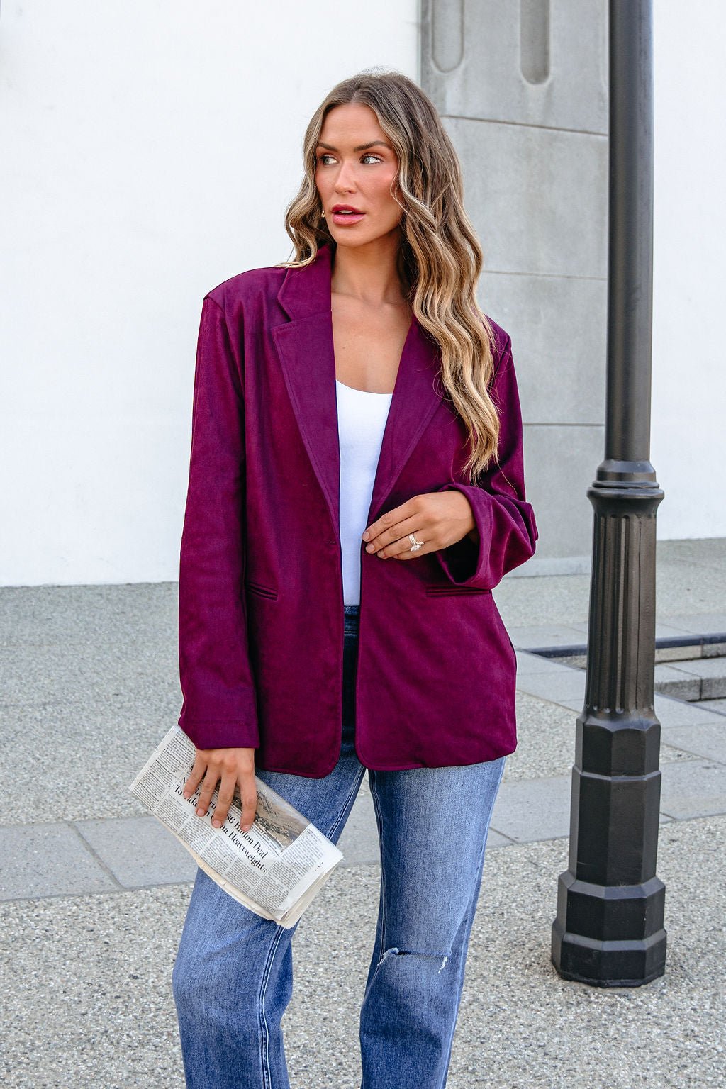 Woman in SHE AND SKY ST1741 wine suede oversized blazer and jeans holds a folded newspaper by a streetlamp.