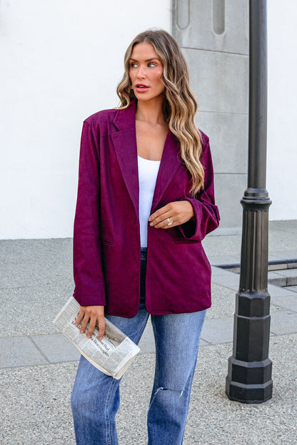 Woman in SHE AND SKY ST1741 wine suede oversized blazer and jeans holds a folded newspaper by a streetlamp.